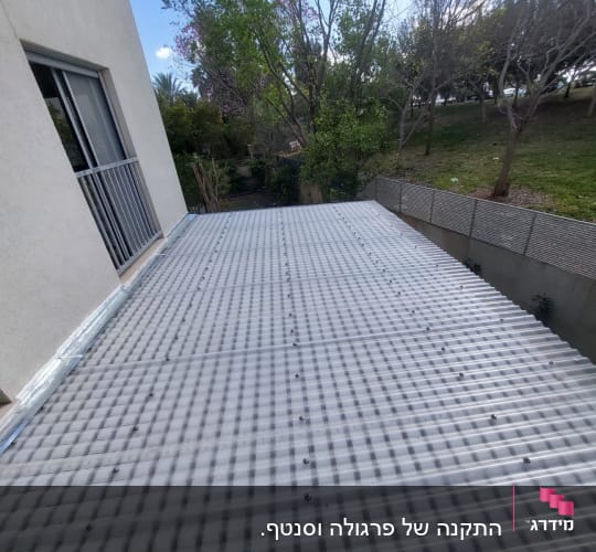 גג פלסטיק גלי מחובר למבנה ליד גינה